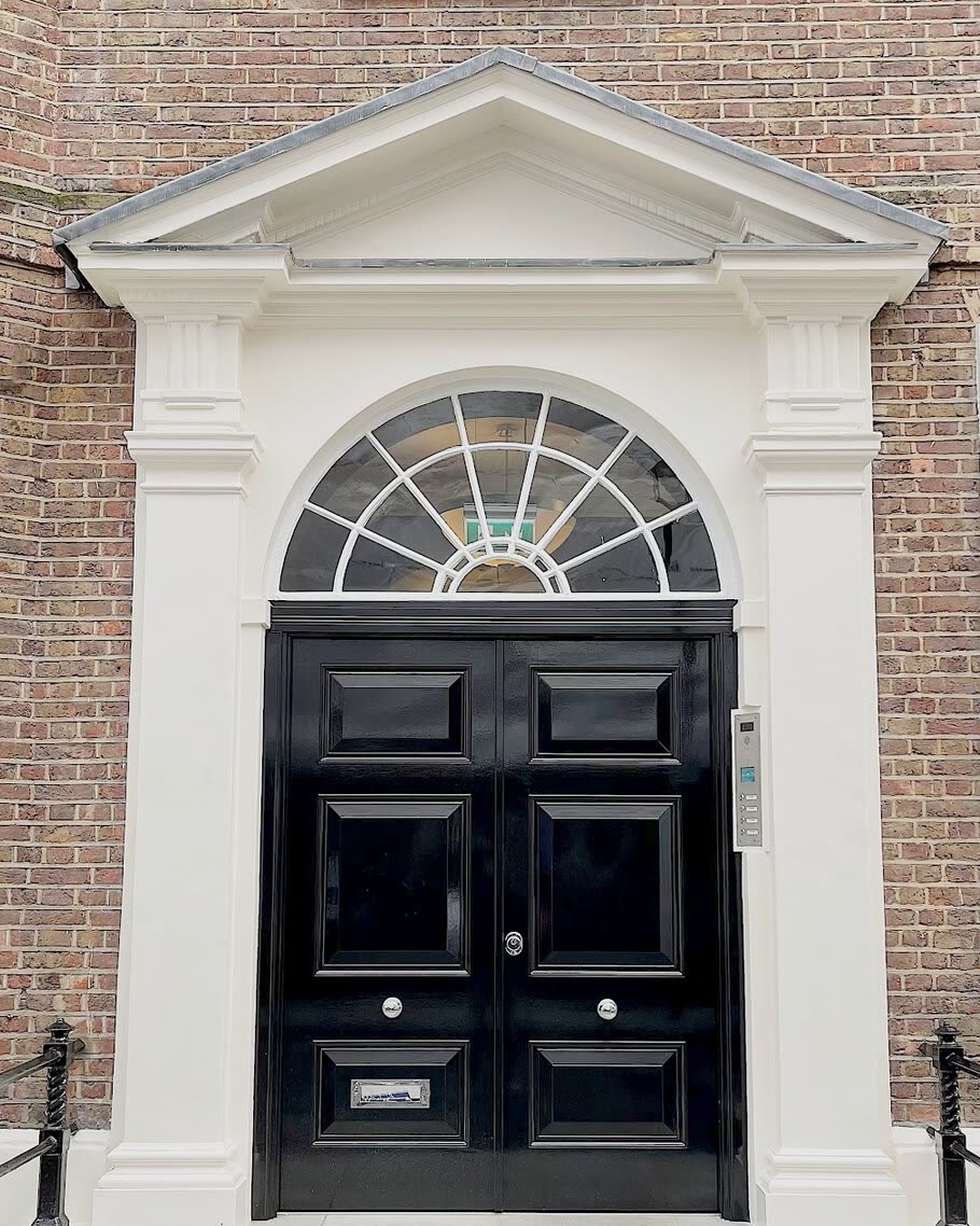 Gloss black Georgian double entry door with a fanlight, set in a pedimented stone portico.