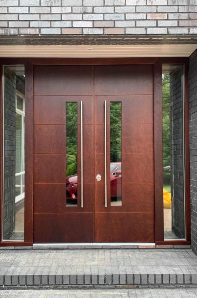 High security entry door in stained hardwood, a matched pair with slim vertical vision panels and full-height glass sidelights, set in a grey brick porch.