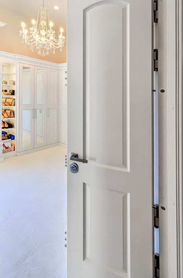 White panic room door standing open, showing the passive bolts along the hinge edge.