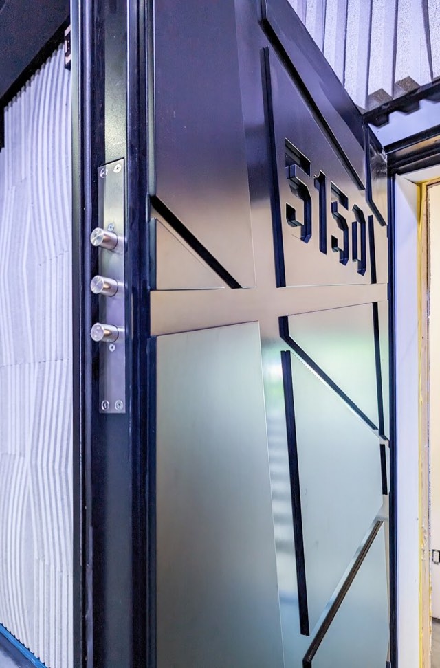 Vault room door standing open, showing three hardened steel bolts projecting from the strike edge and the frameless glass panel beyond.