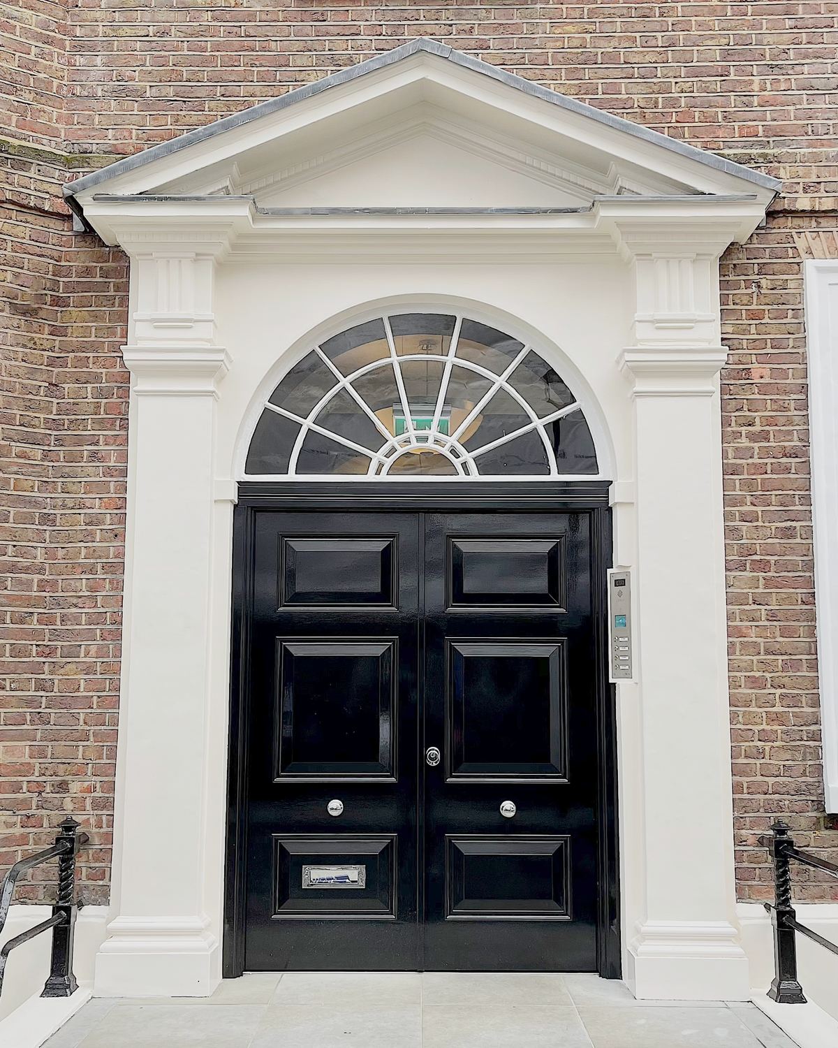 Gloss black Georgian double entry door with a fanlight, set in a pedimented stone portico.