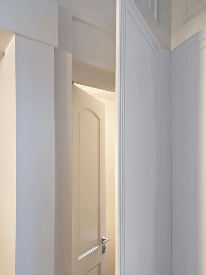 Painted door set into a milled paneled wall, standing slightly open.